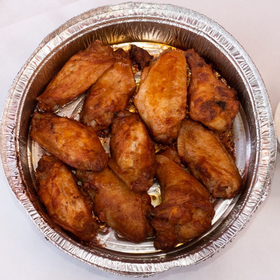 A foil pan filled with crispy, golden-brown chicken wings, ready to be served from Fiesta Pizza.