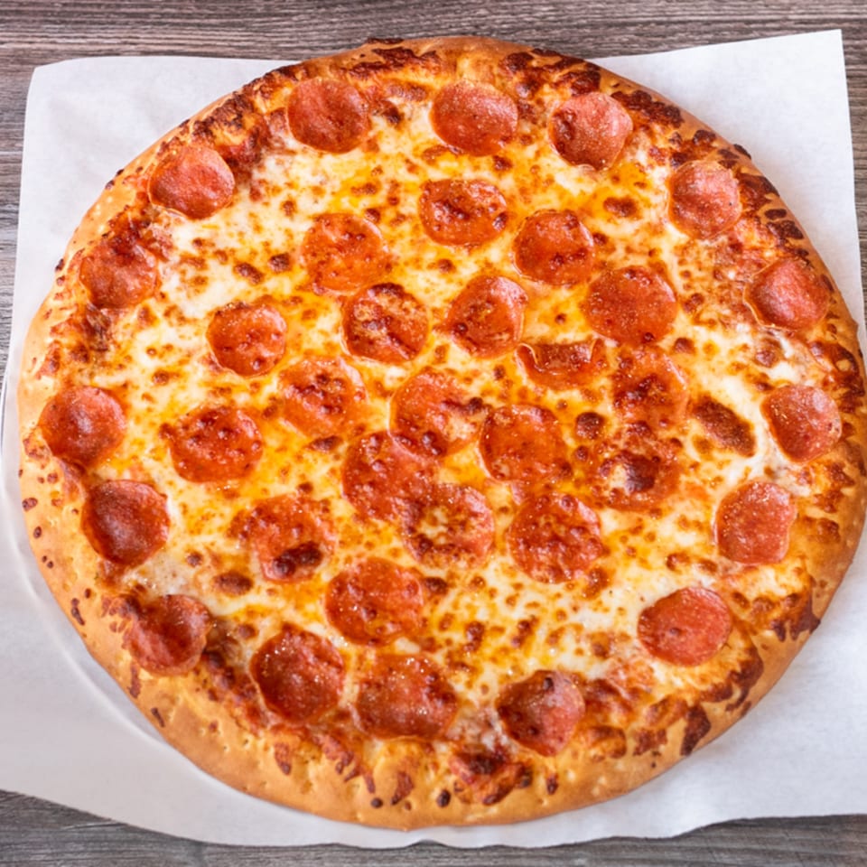 A whole pepperoni pizza from Fiesta Pizza, with melted cheese and crispy crust, on parchment paper.