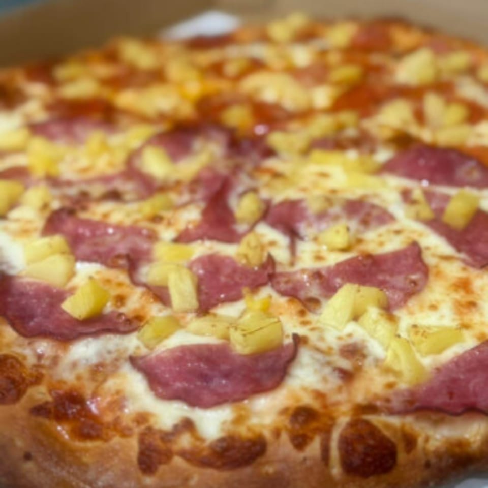 Close-up of a Fiesta Pizza with pepperoni, pineapple, and melted cheese.