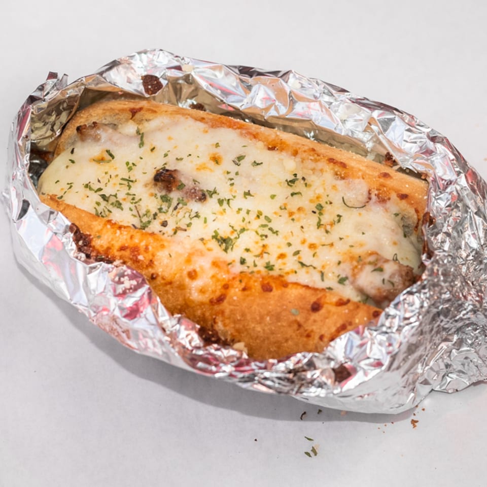 A cheesy Fiesta Pizza sub sandwich, wrapped in foil, with melted cheese and herbs on top.