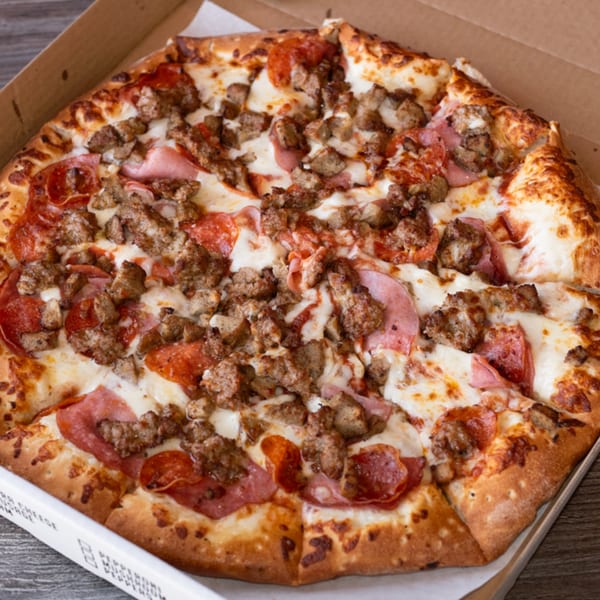 A Fiesta Pizza meat lover's pizza, topped with pepperoni, ham, and sausage, in a cardboard box.